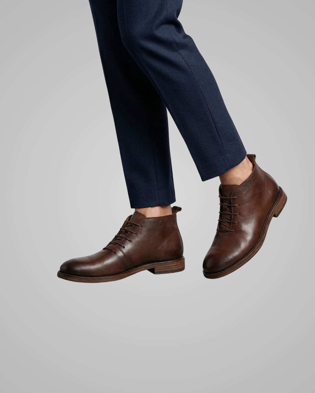 Brown leather shoes worn with navy pants on a gray background