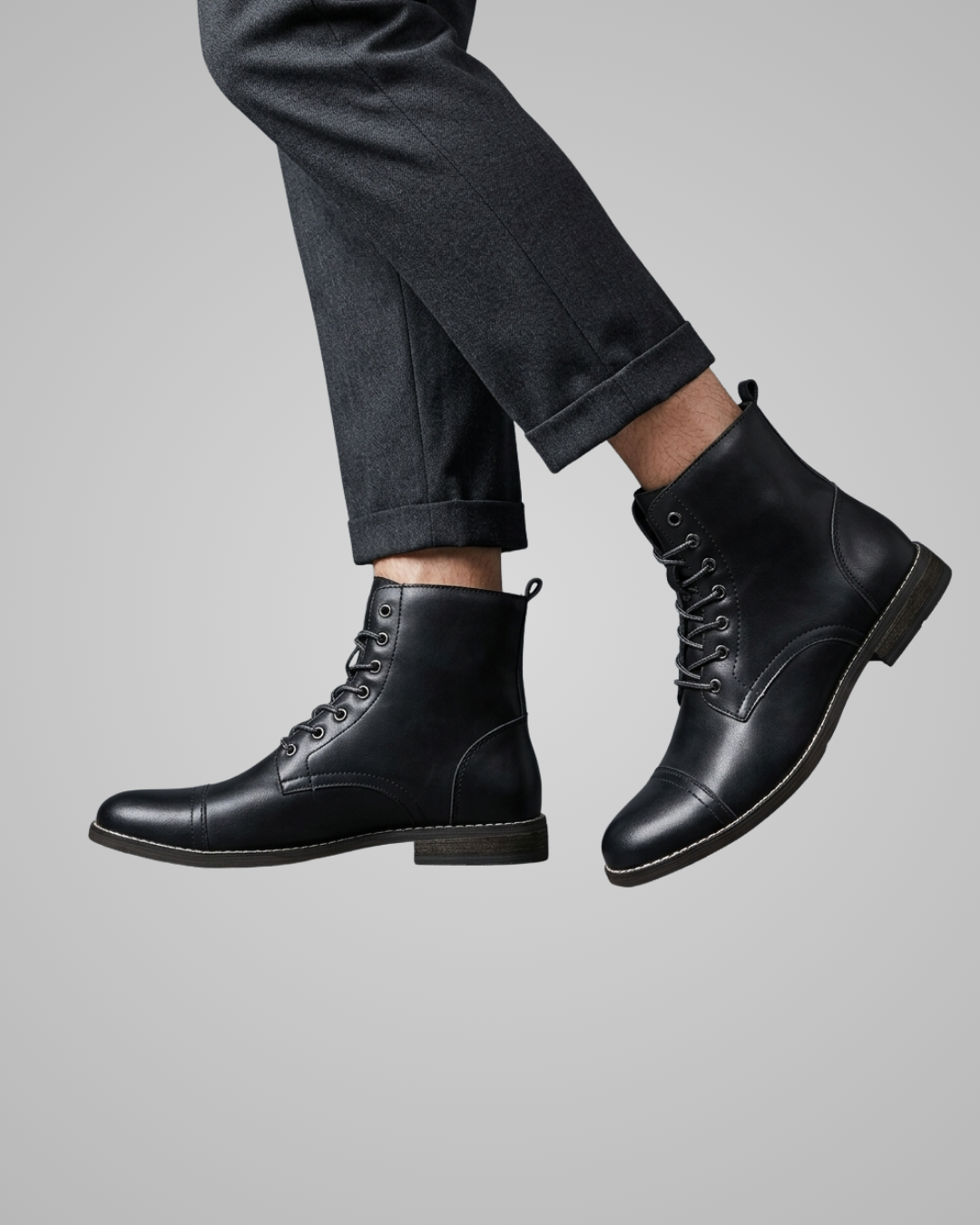 Black leather boots worn with dark pants on a gray background