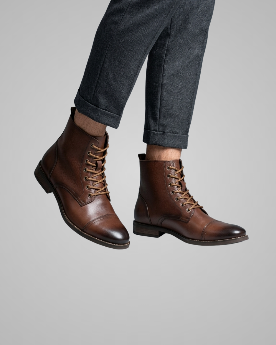 Brown leather boots worn with dark pants on a gray background