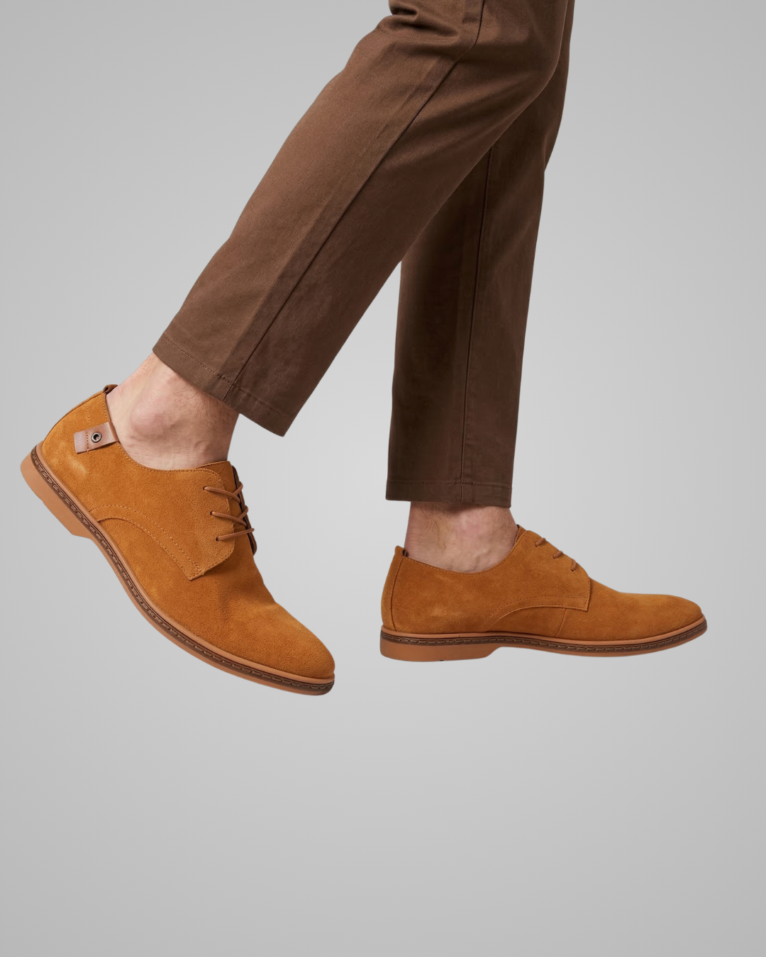 Brown suede shoes worn with brown pants on a gray background