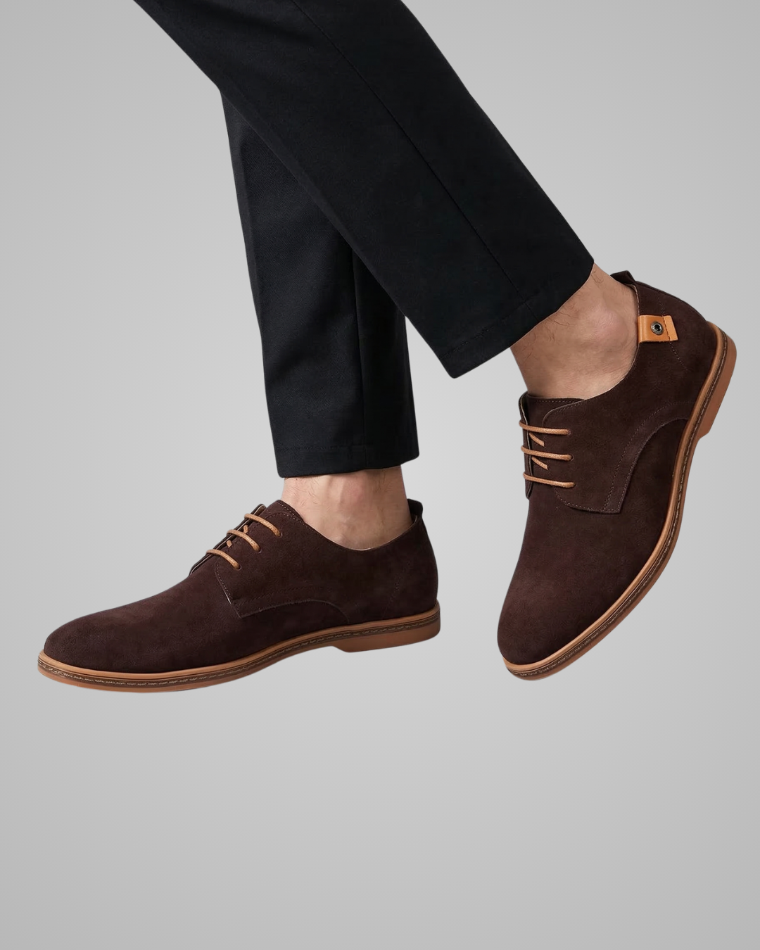Brown suede shoes worn with black pants on a gray background