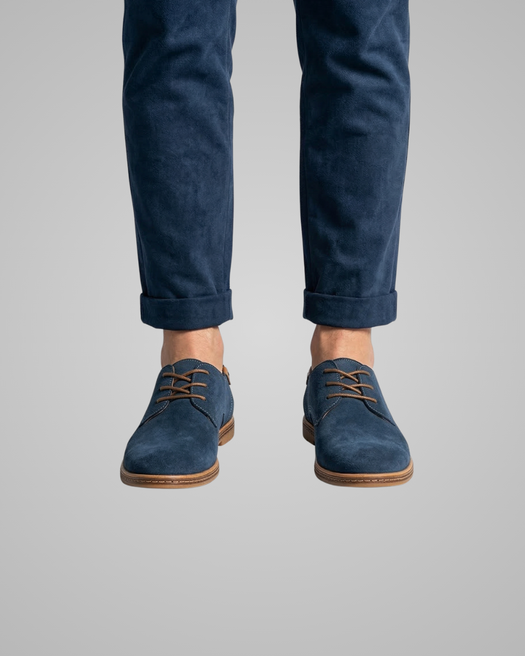 Blue suede shoes worn with rolled-up navy pants on a gray background