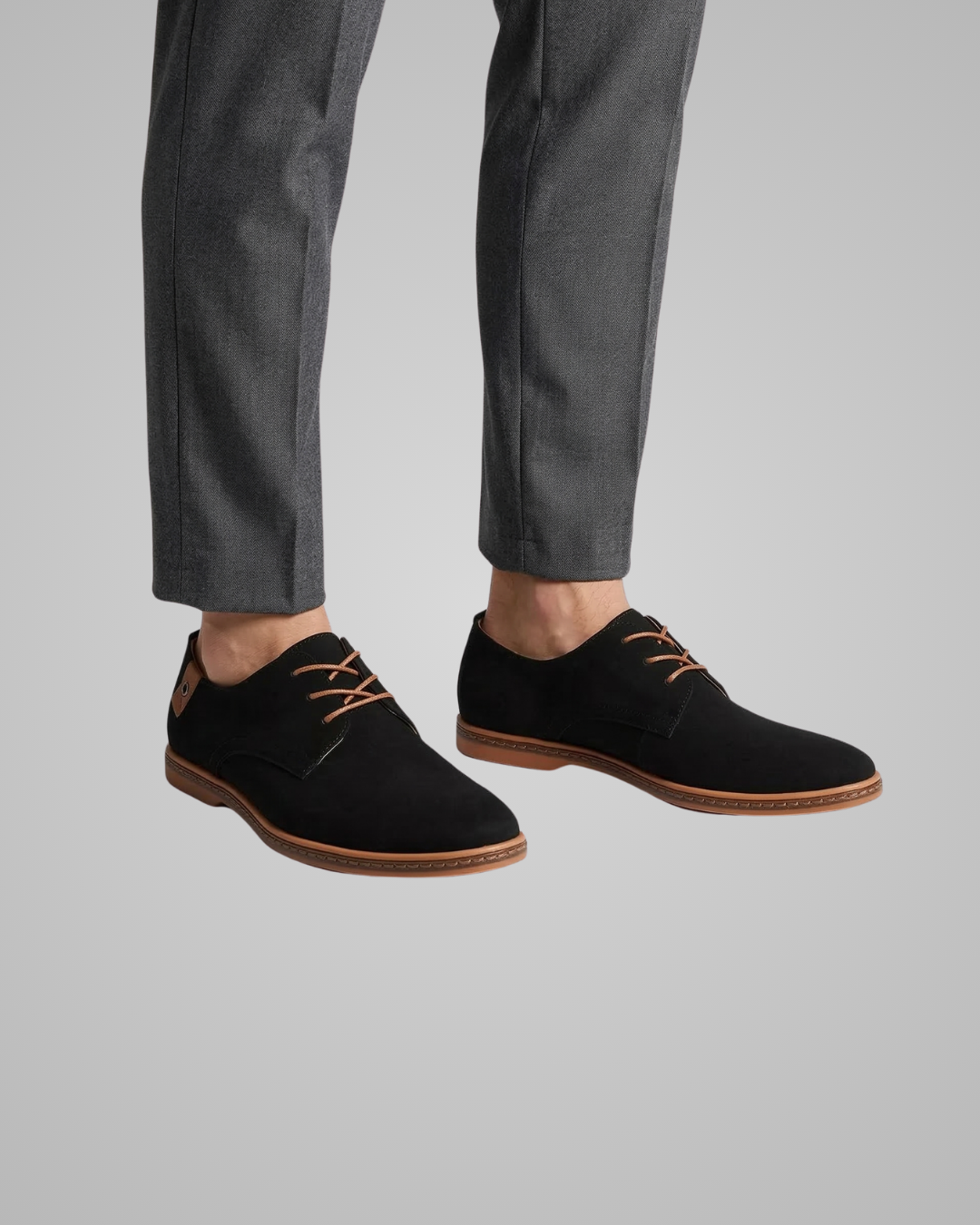 Black shoes with brown soles worn with gray pants on a light gray background