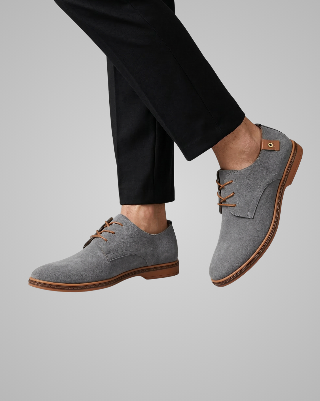 Gray suede shoes with brown soles worn by a person on a gray background