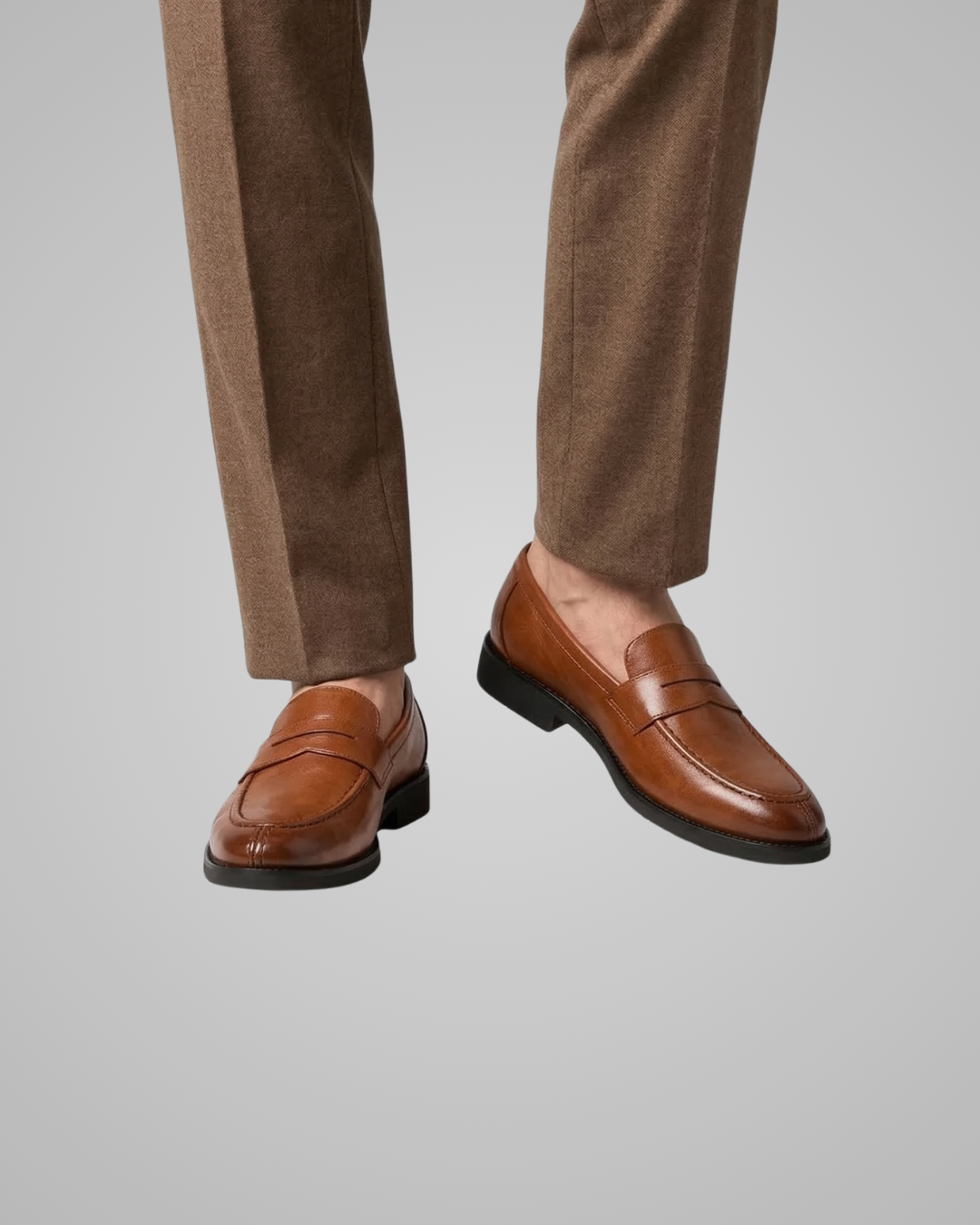 Brown loafers worn with brown pants on a light gray background