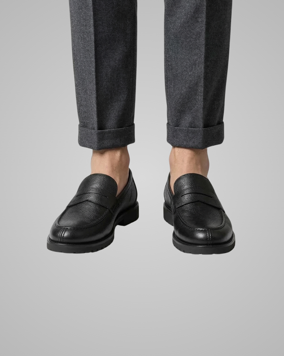 Black loafers worn with gray pants on a light gray background