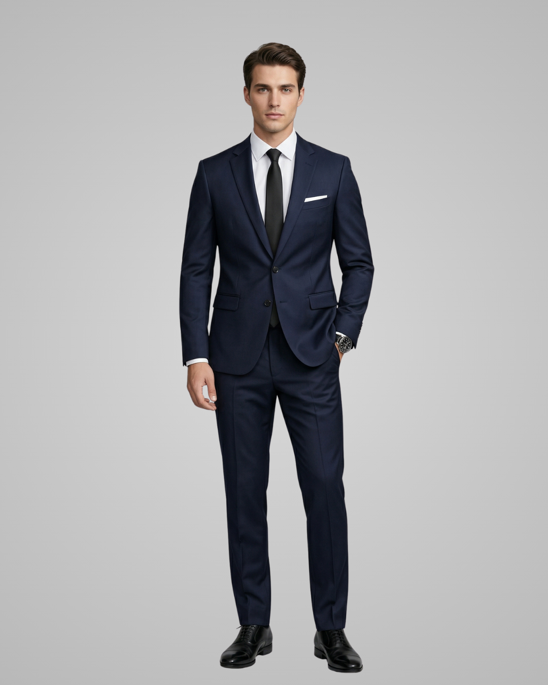 Man wearing a navy blue suit with a white shirt and black shoes on a gray background