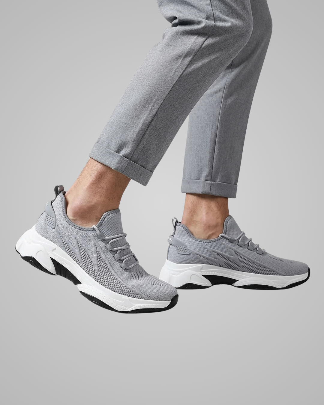 Gray sneakers worn with gray pants on a light gray background