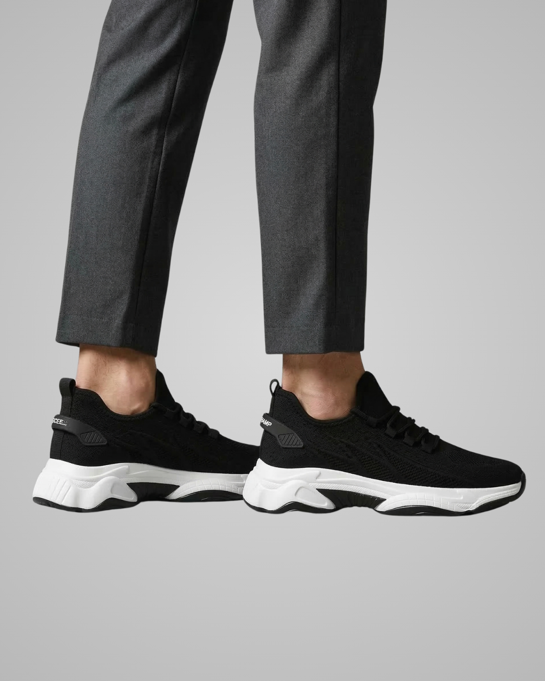 Black sneakers worn with gray pants on a light gray background