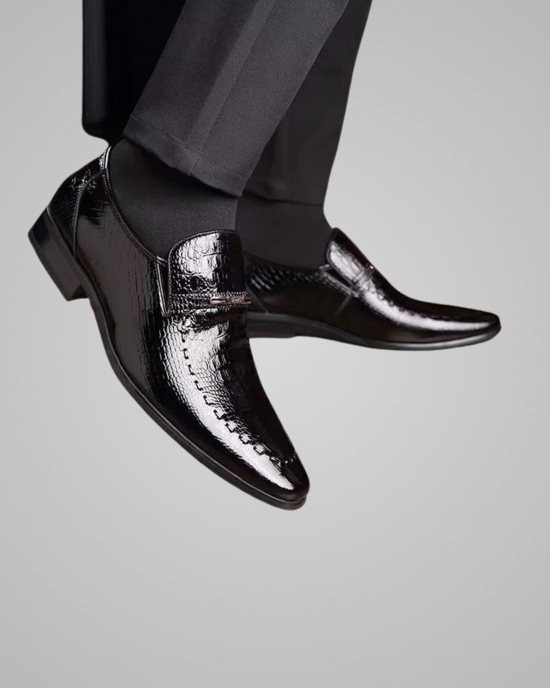 Black dress shoes with a textured pattern worn by a person on a light gray background