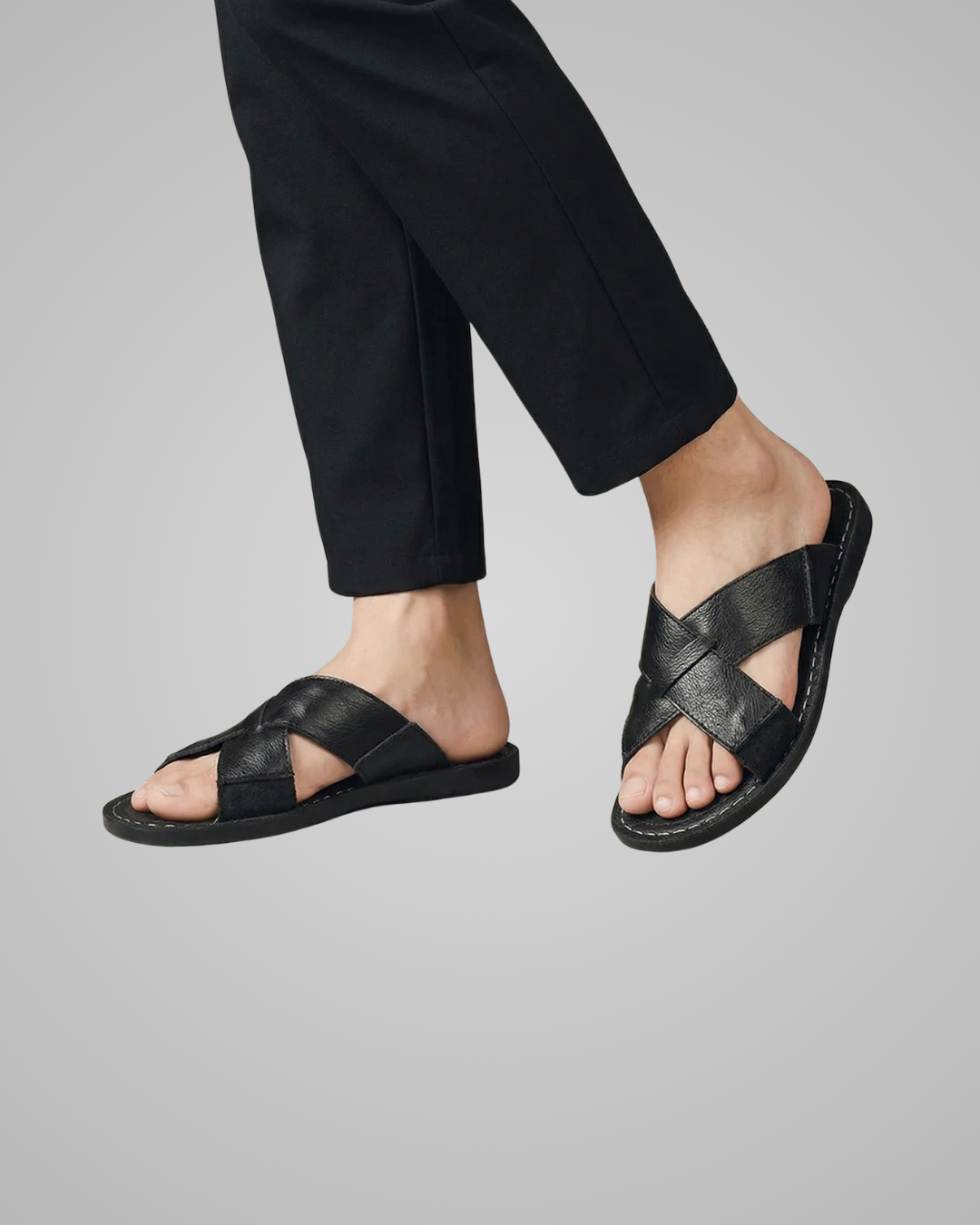 Person wearing black leather sandals on a gray background