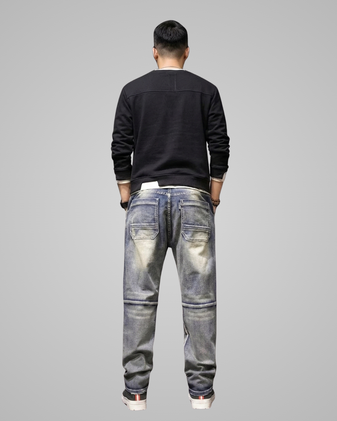 Person wearing a black sweater and distressed jeans on a gray background