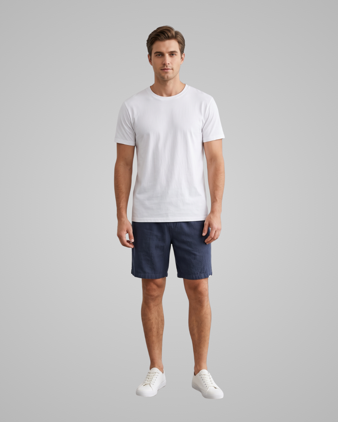 A man modeling a plain white short-sleeve crewneck t-shirt, paired with navy blue shorts and white sneakers, against a solid light gray background.