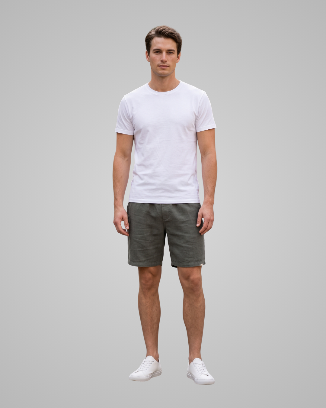 A man modeling a white crew-neck t-shirt and olive green shorts against a solid gray background.