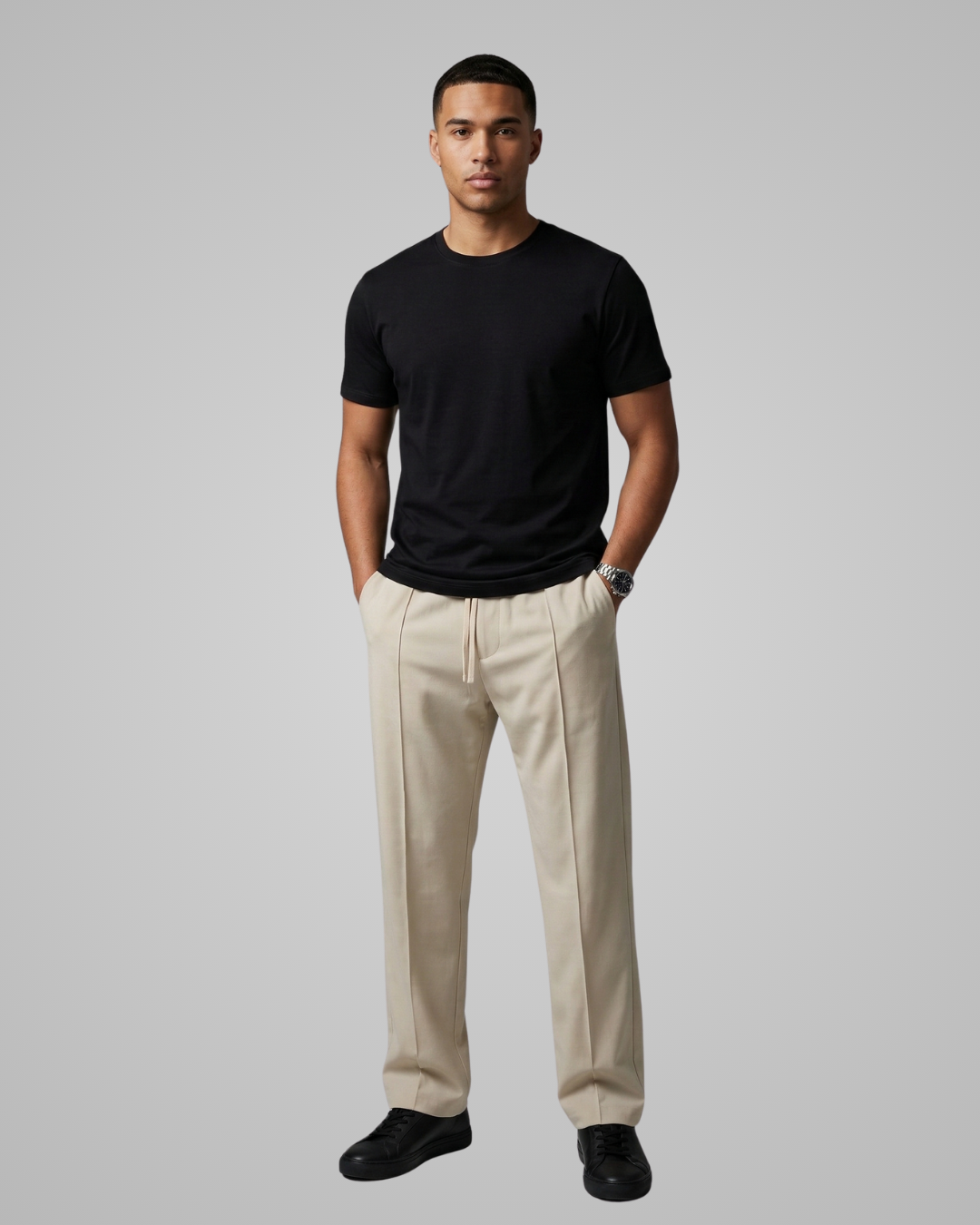 Man wearing a black t-shirt and beige pants against a gray background