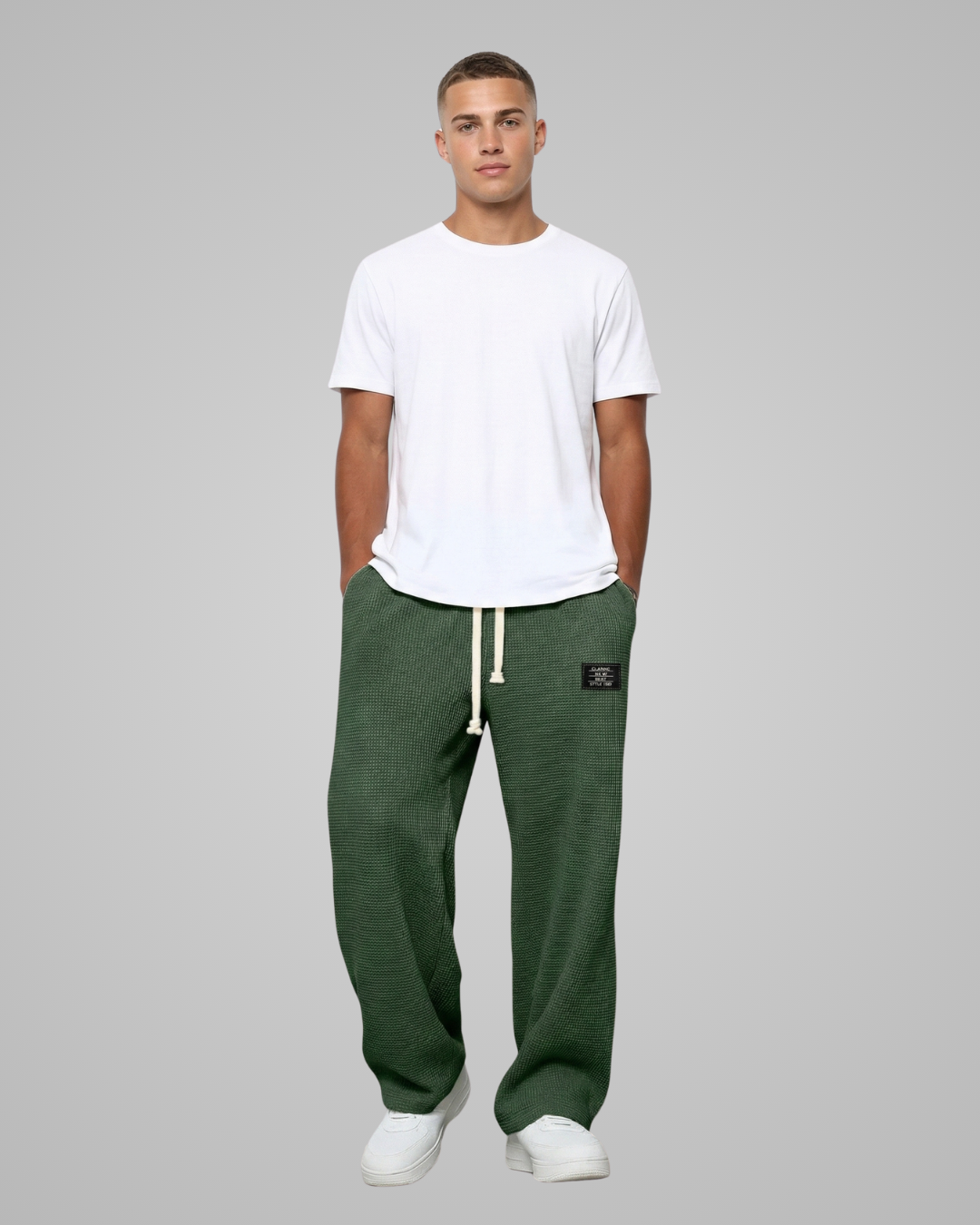 Man wearing a white t-shirt and green sweatpants on a gray background