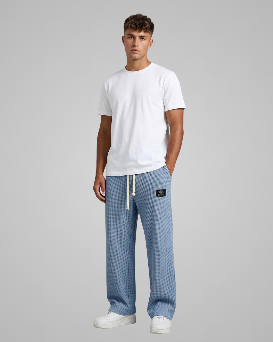 Man wearing a white t-shirt and light blue pants on a gray background