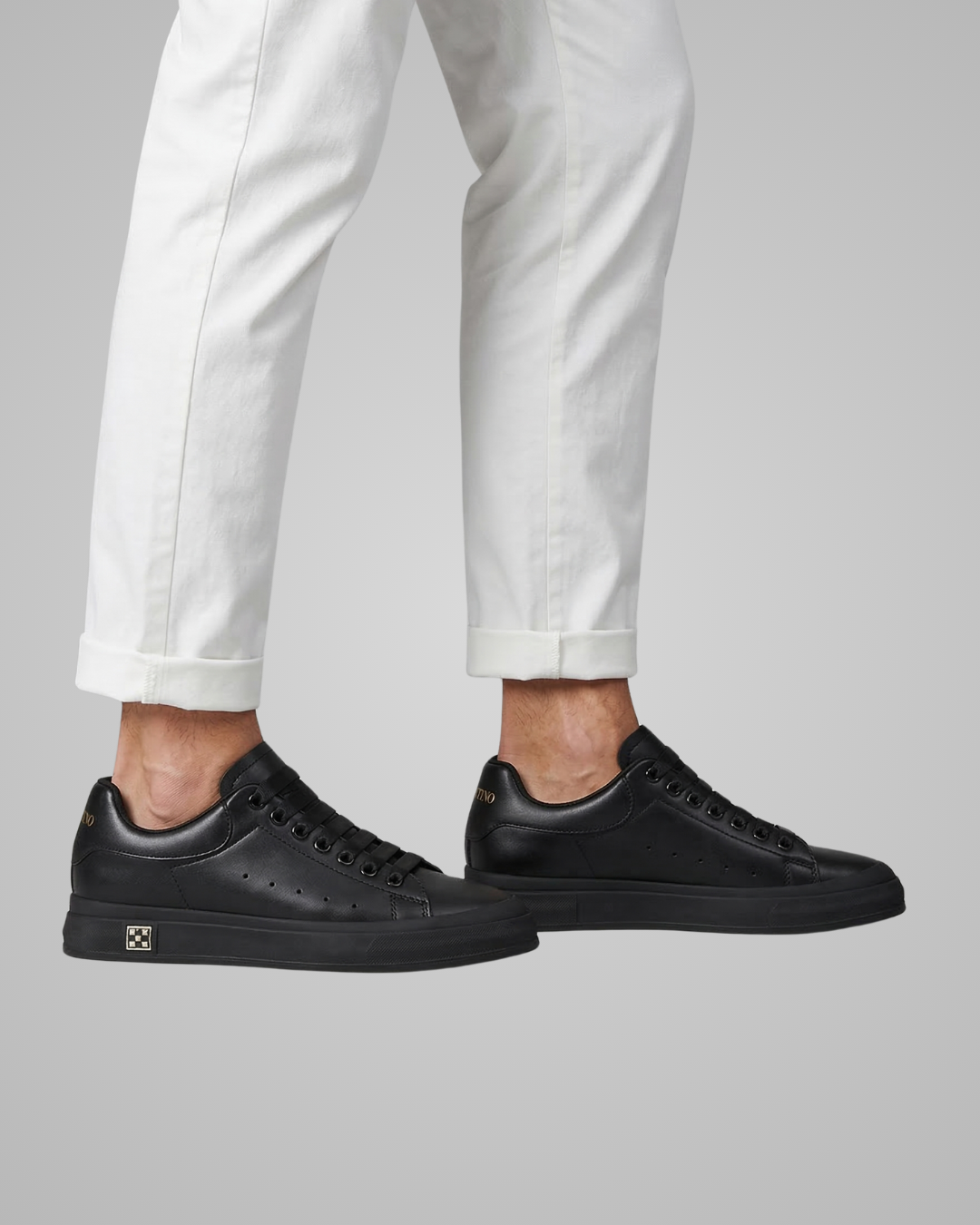 Black sneakers worn with white pants on a gray background