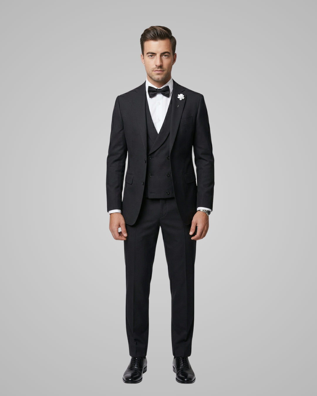 Man wearing a black tuxedo with a white shirt and bow tie on a gray background