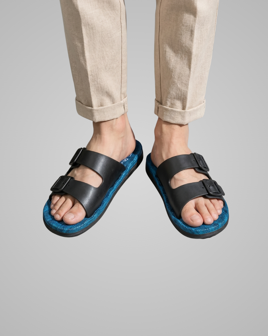Black and blue sandals worn with light-colored pants on a gray background