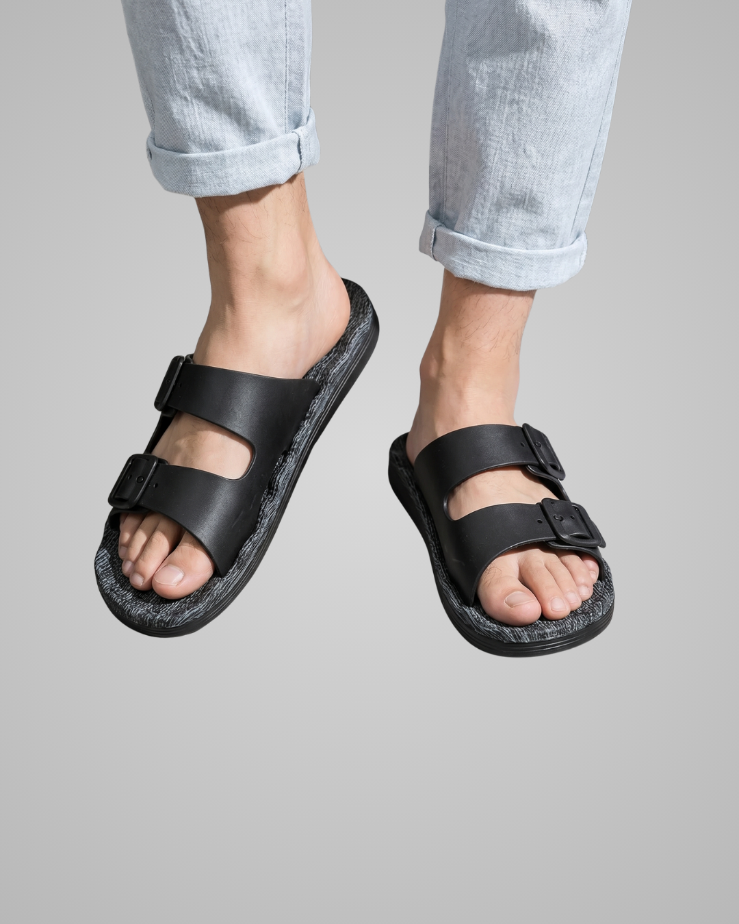 Black sandals worn with light blue jeans on a gray background