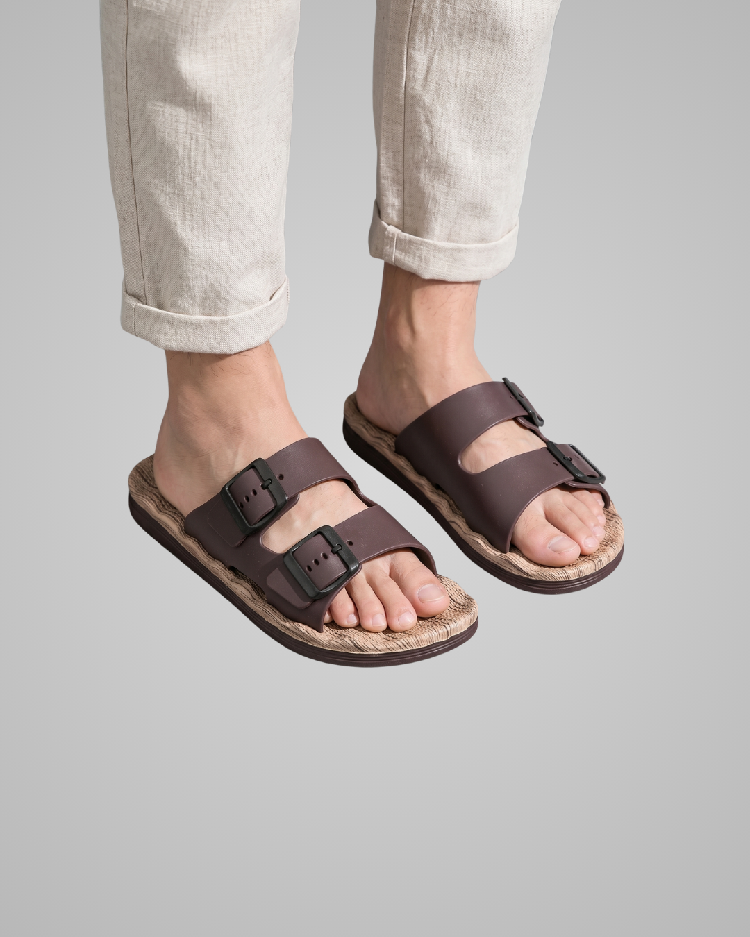 Brown sandals worn with light-colored pants on a gray background