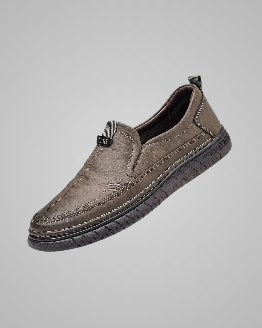 A single slip-on casual shoe in taupe-brown textured leather with a dark sole, shown floating against a solid gray background.