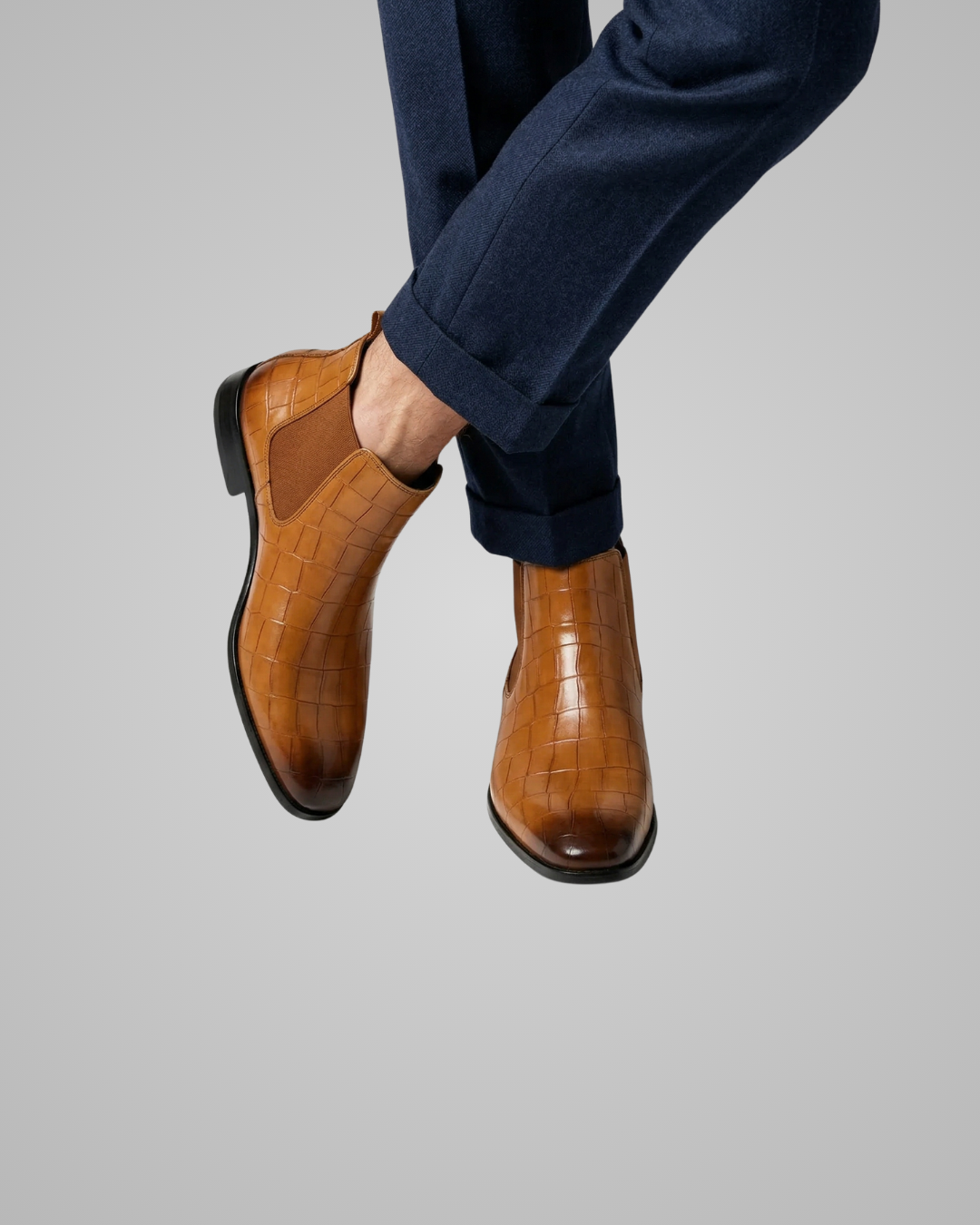 Brown leather shoes worn with navy pants on a gray background