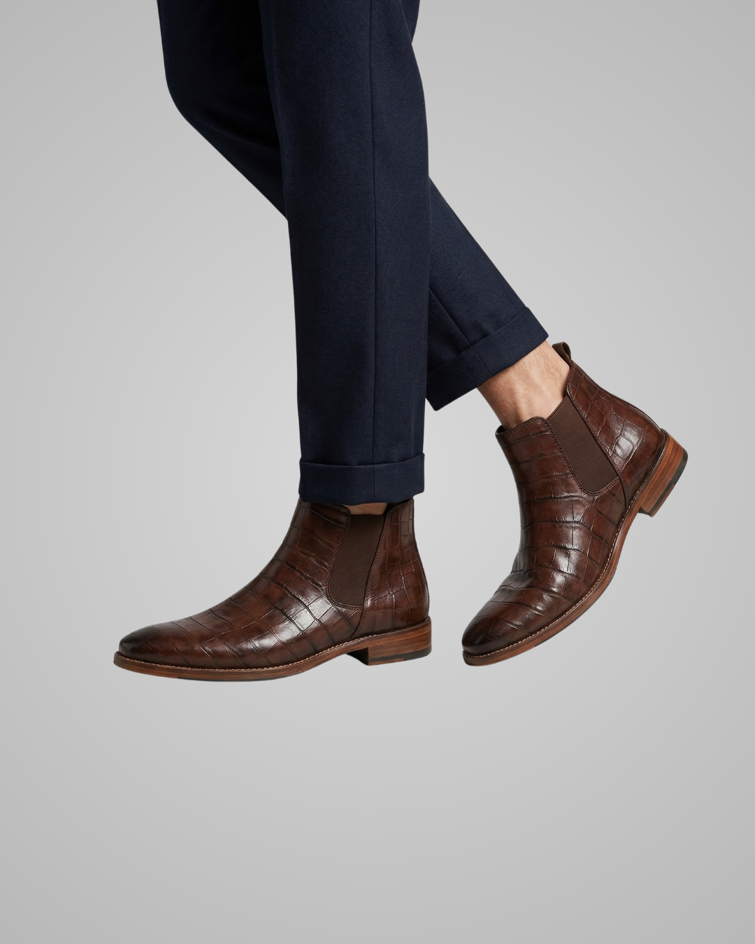 Brown leather boots worn with navy pants on a gray background