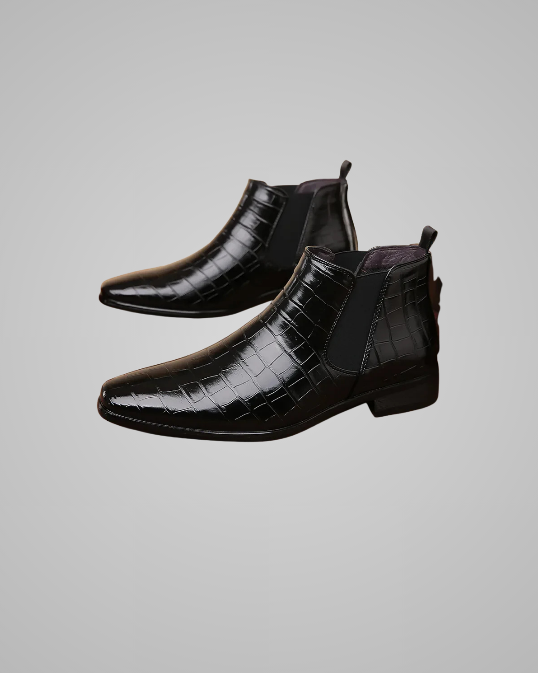 Black crocodile-patterned leather boots on a gray background