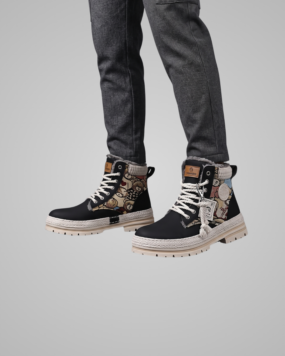 Black high-top sneakers with patterned design worn with gray pants on a light gray background