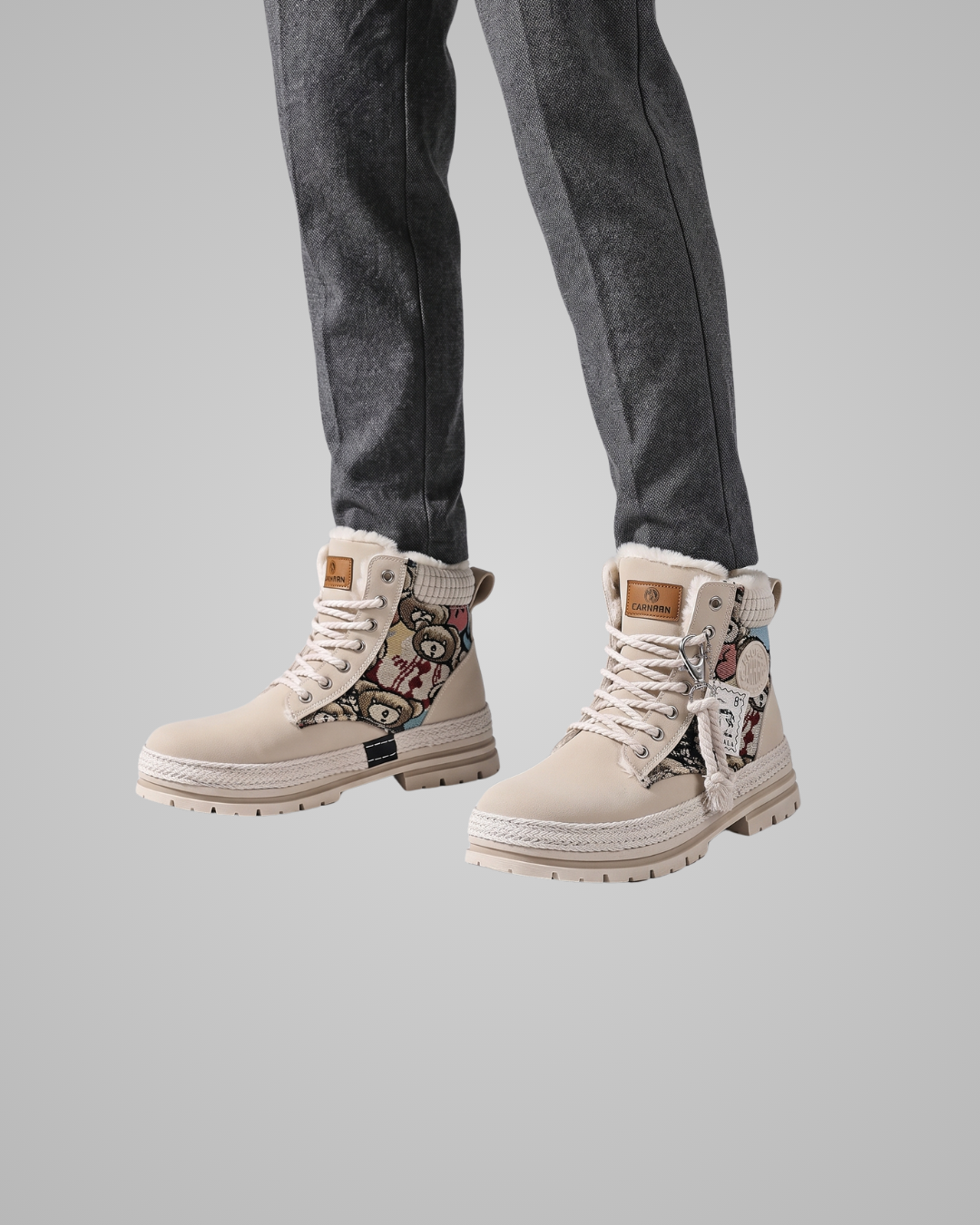 Beige high-top boots with patterned design worn with dark jeans on a gray background