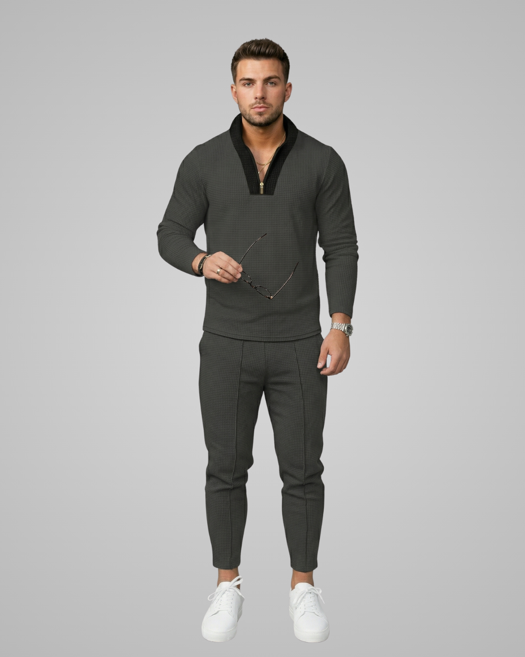 Man wearing a dark gray outfit with a V-neck sweater and pants on a light gray background