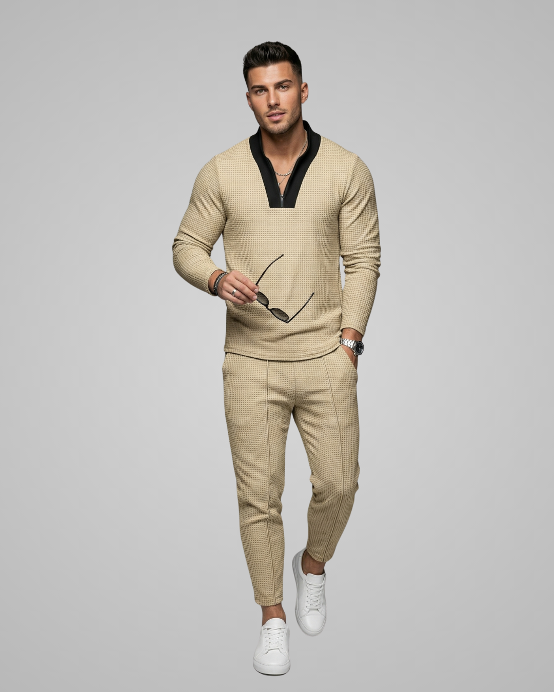 Man wearing a beige sweater and pants with white sneakers on a gray background