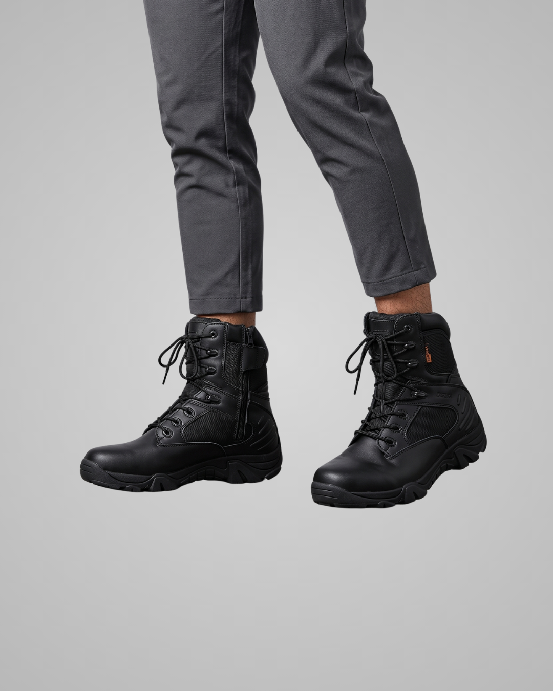 A pair of black lace-up tactical boots worn with dark gray pants, shown from the calves down against a solid light gray background.