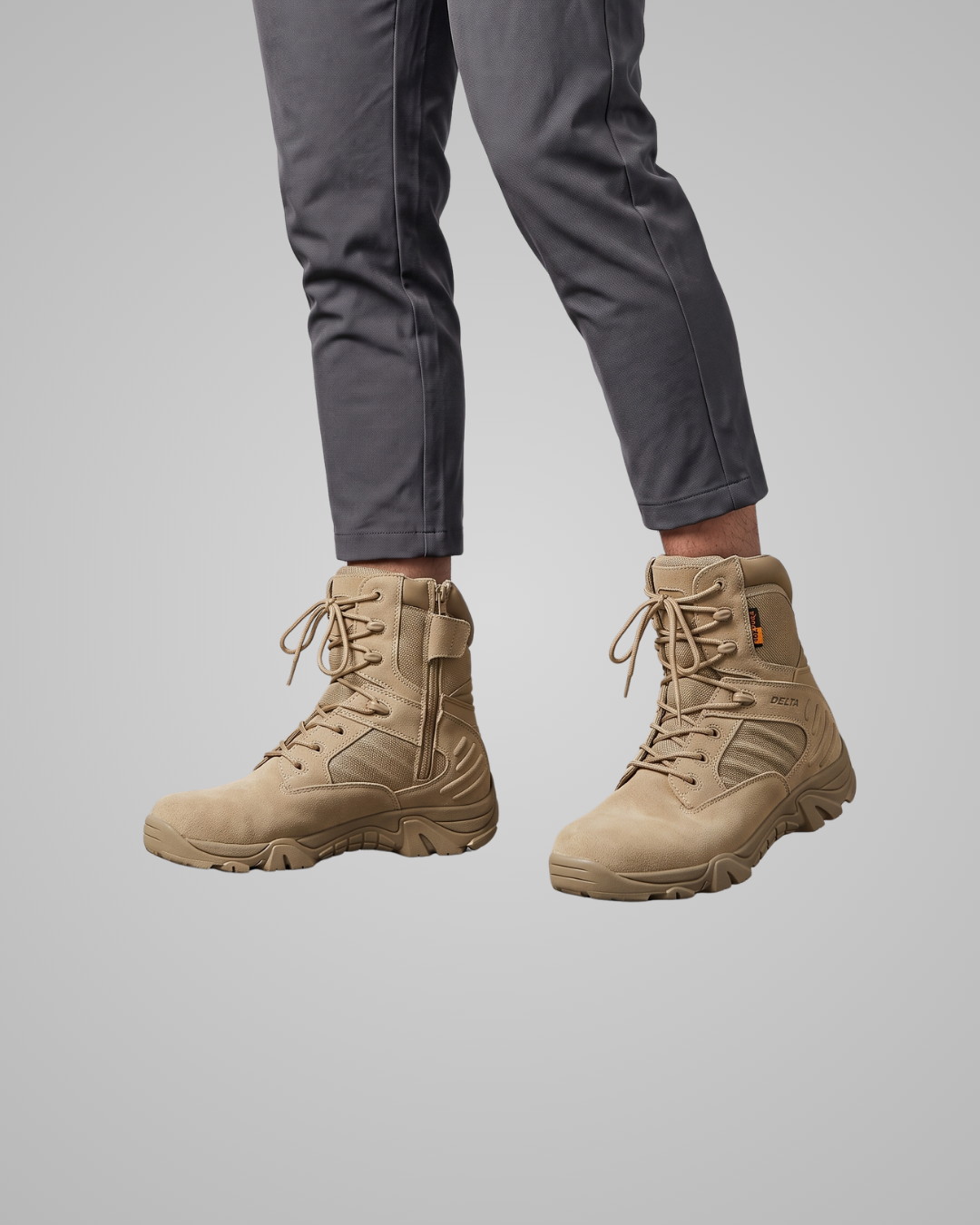 A pair of tan tactical combat boots with gray pants shown on a model's feet against a solid gray background.