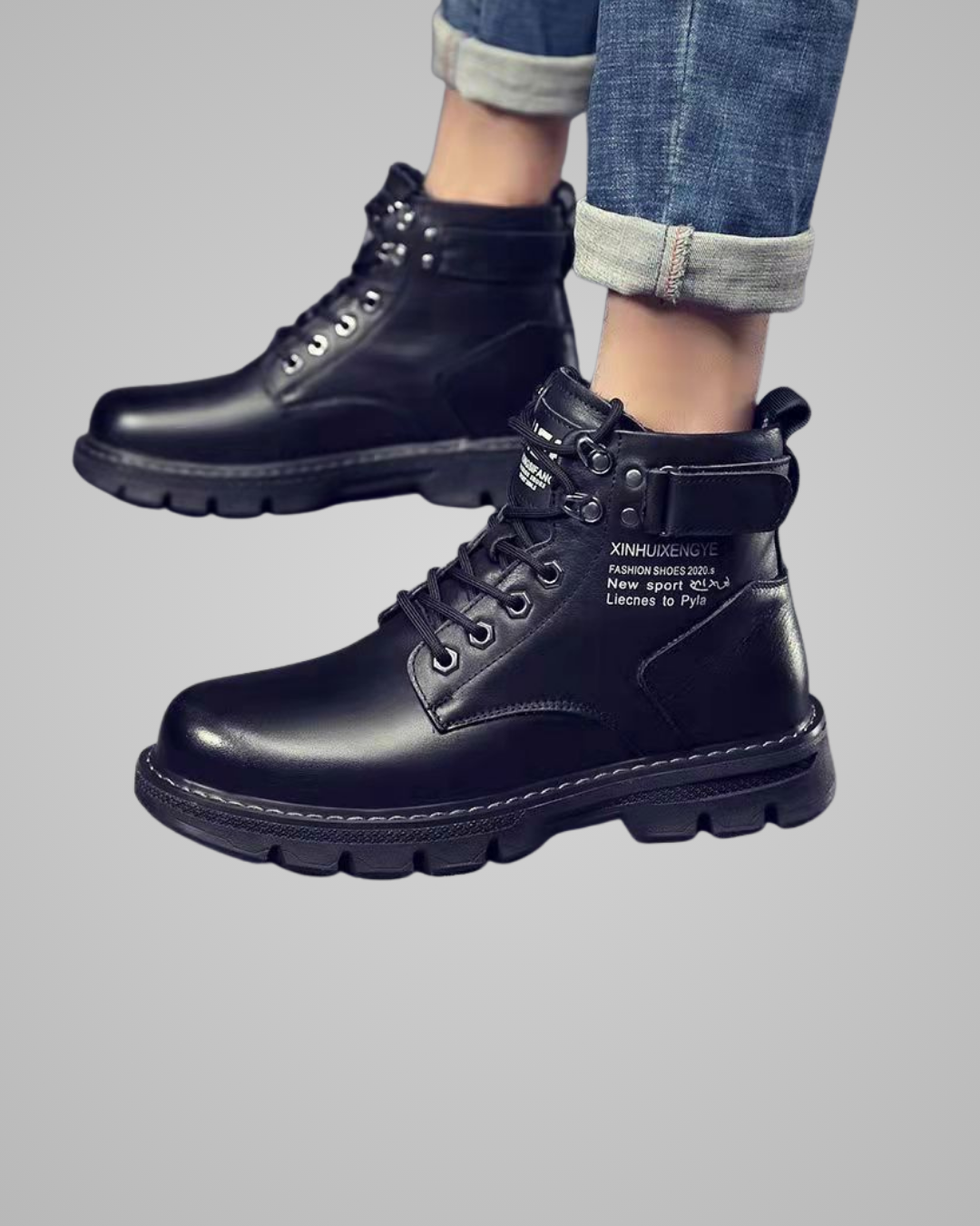 Black leather boots worn with rolled-up jeans on a gray background