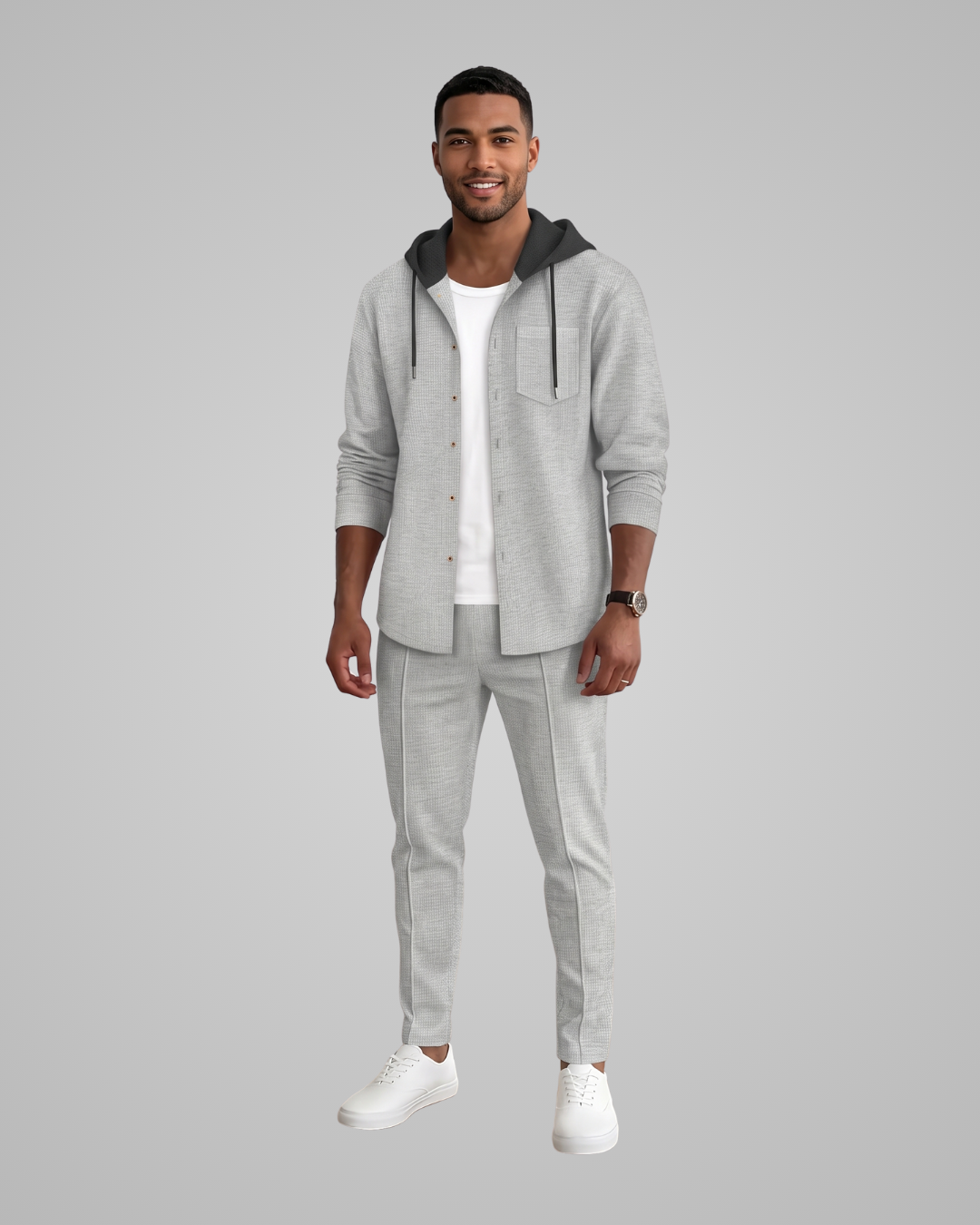 A man modeling a light gray heathered lounge set consisting of a hooded button-front cardigan and matching jogger pants, styled over a white t-shirt and white sneakers against a solid gray background.