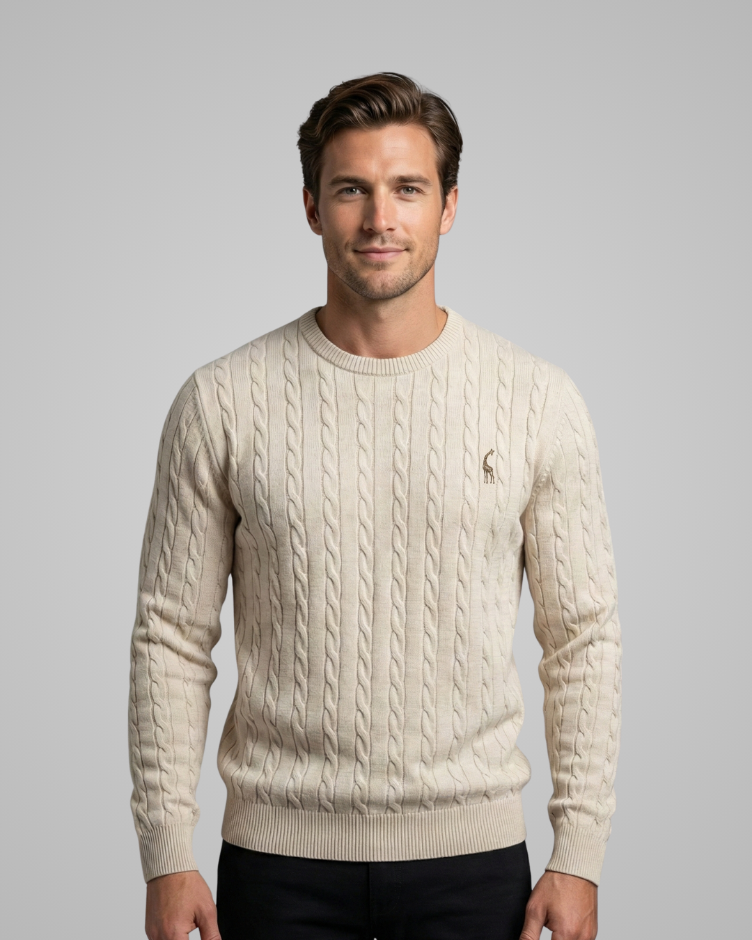 Man wearing a cream cable knit sweater with a logo on a gray background
