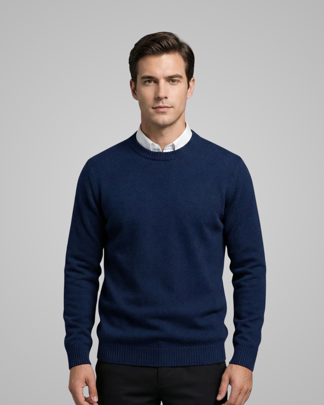 Man wearing a navy blue sweater over a white shirt on a gray background