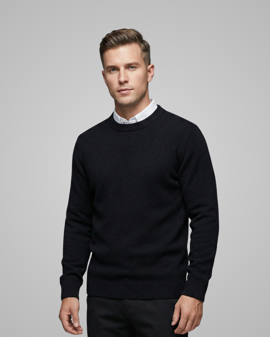 Man wearing a black sweater over a white shirt on a gray background
