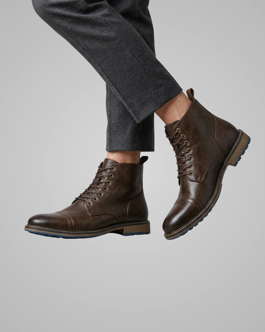 Brown leather boots worn with gray pants on a light gray background