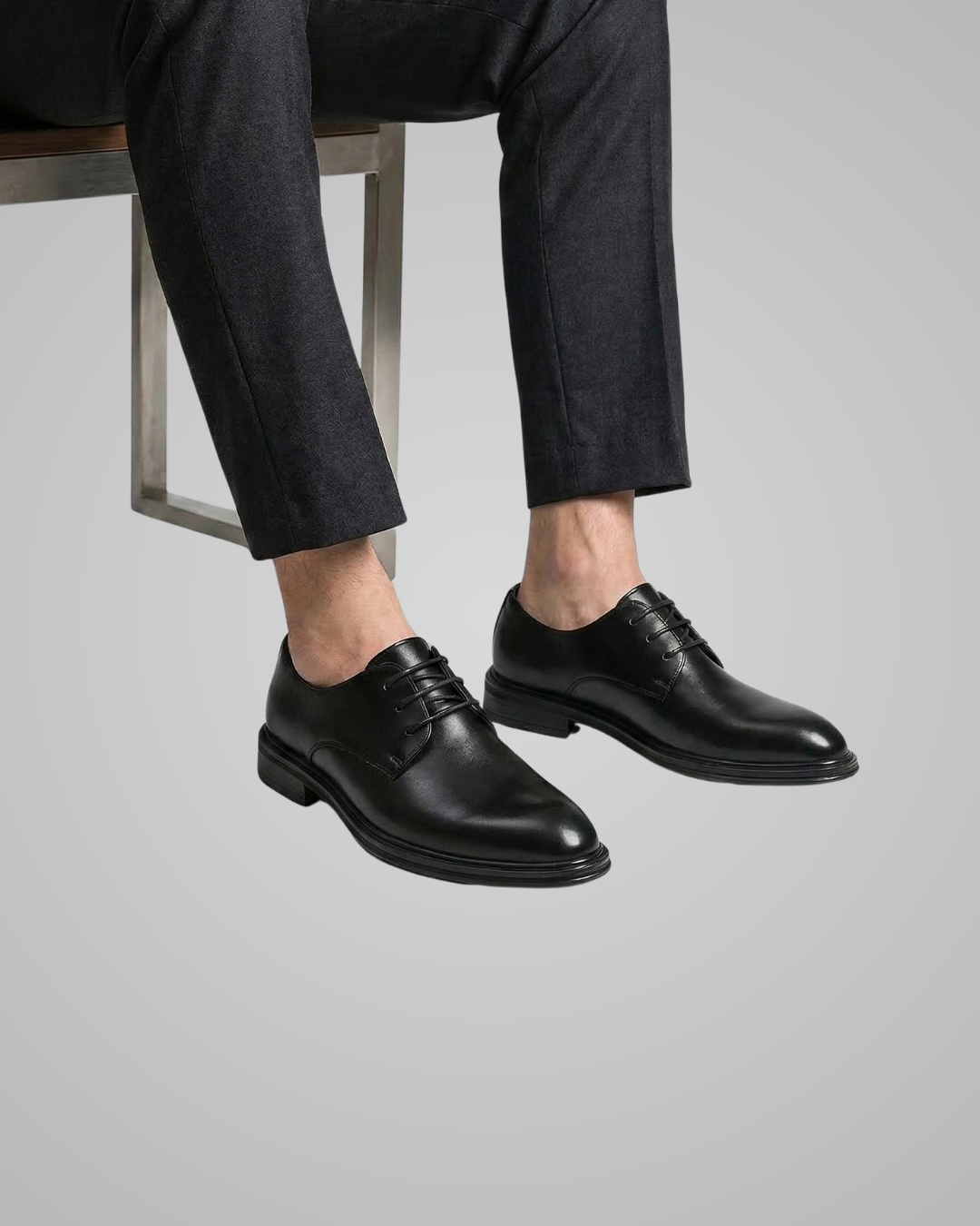 Person wearing black dress shoes and dark pants on a light gray background