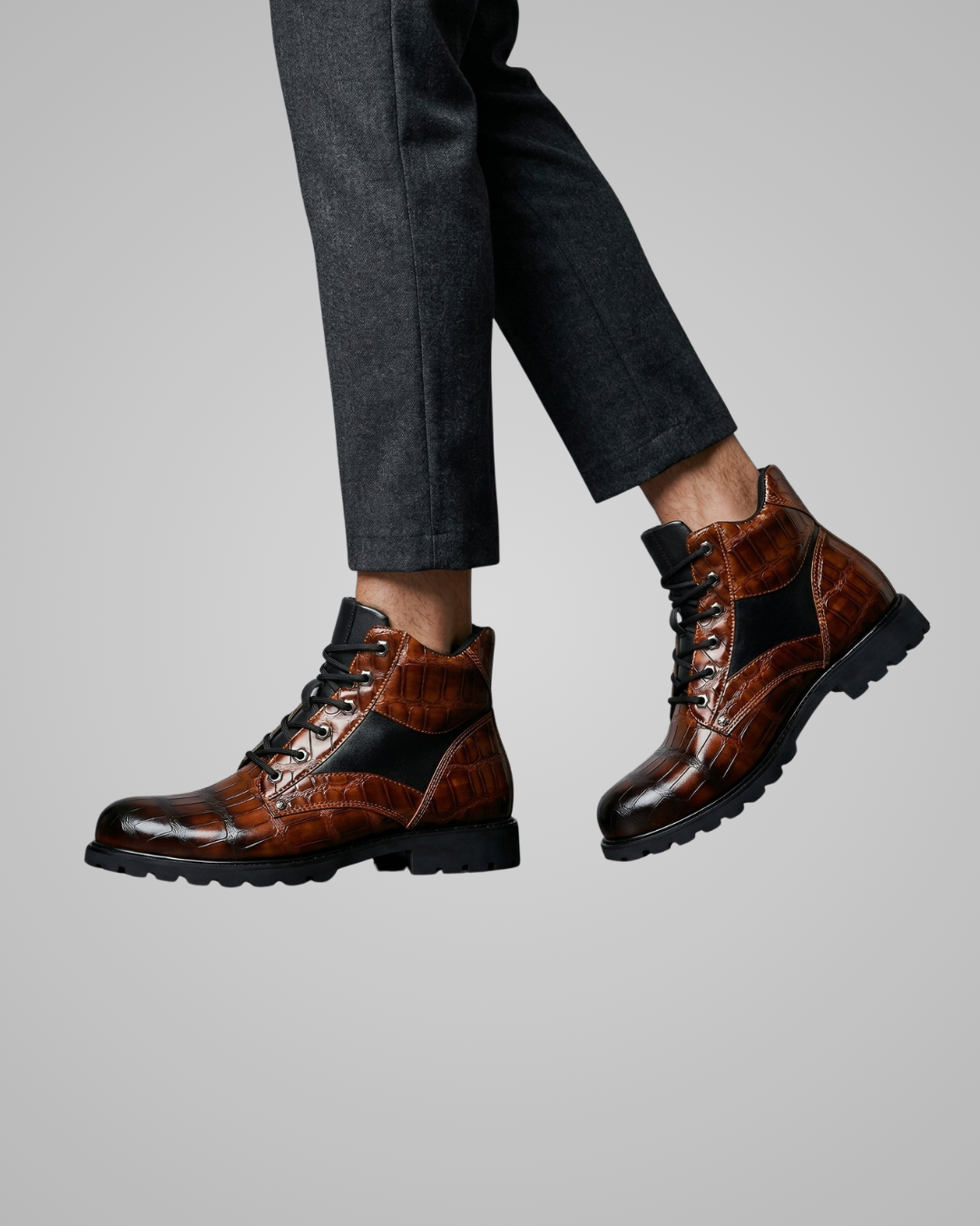 Brown leather boots with black accents worn by a person on a gray background