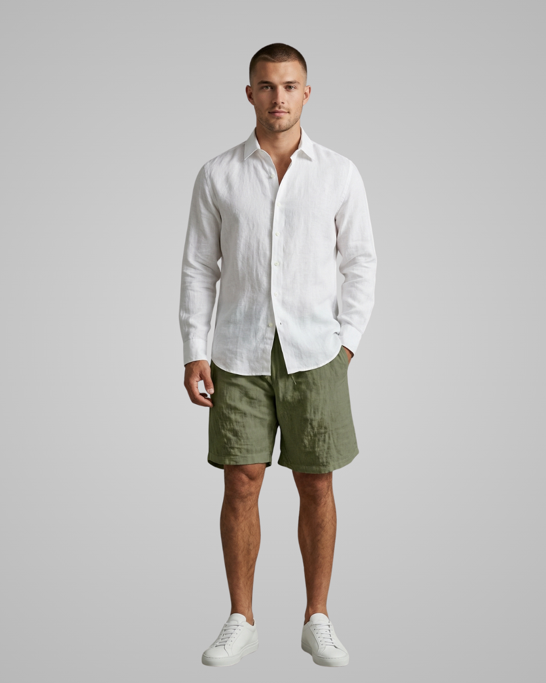 Man wearing a white linen shirt and green shorts on a gray background
