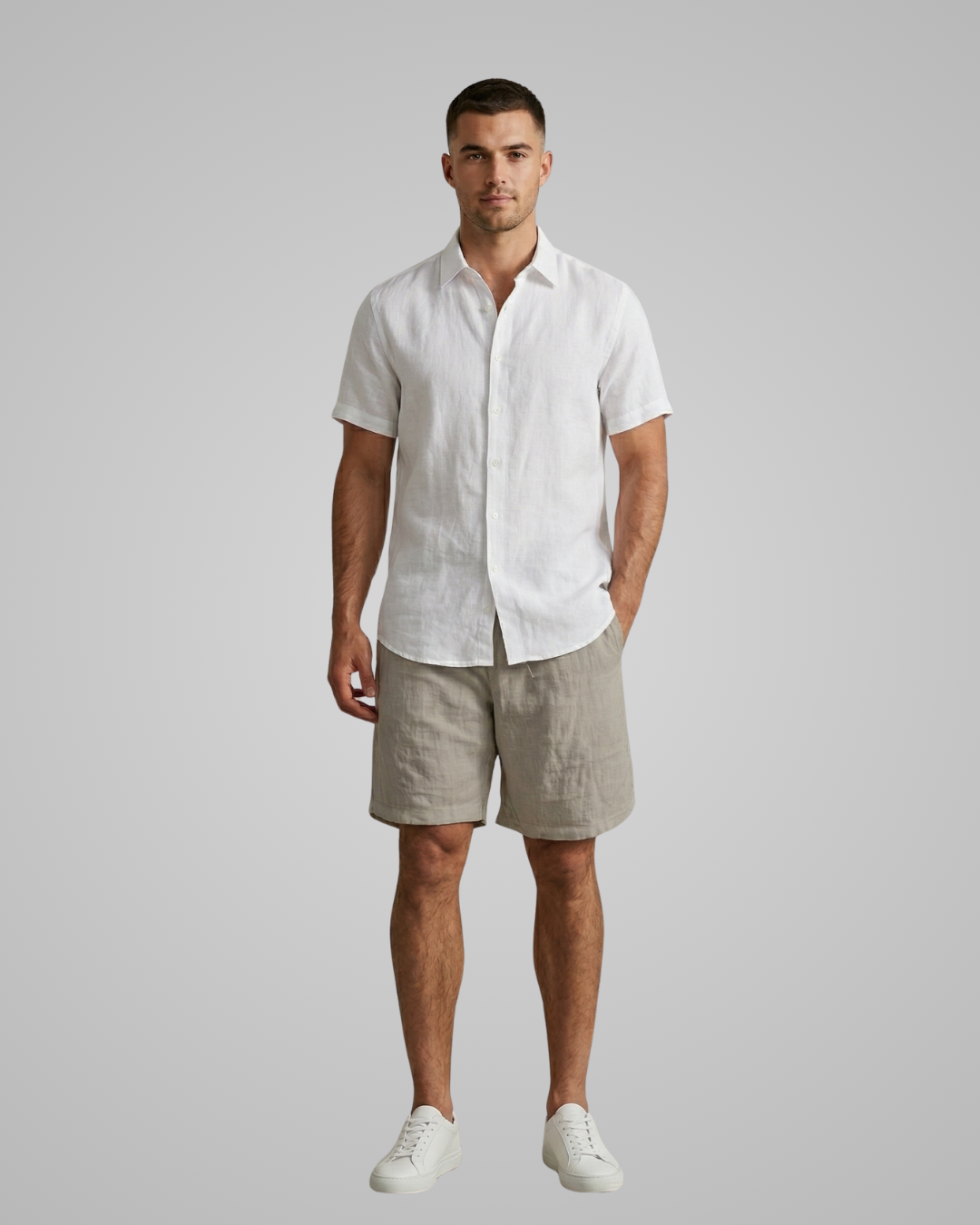 Man wearing a white linen shirt and beige shorts against a gray background