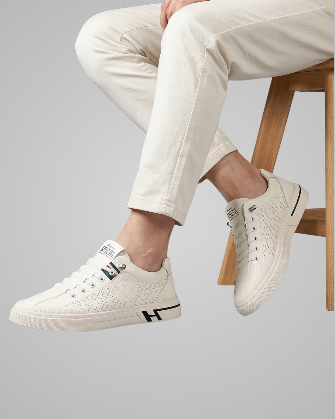 White sneakers with black accents worn by a person sitting on a wooden stool.