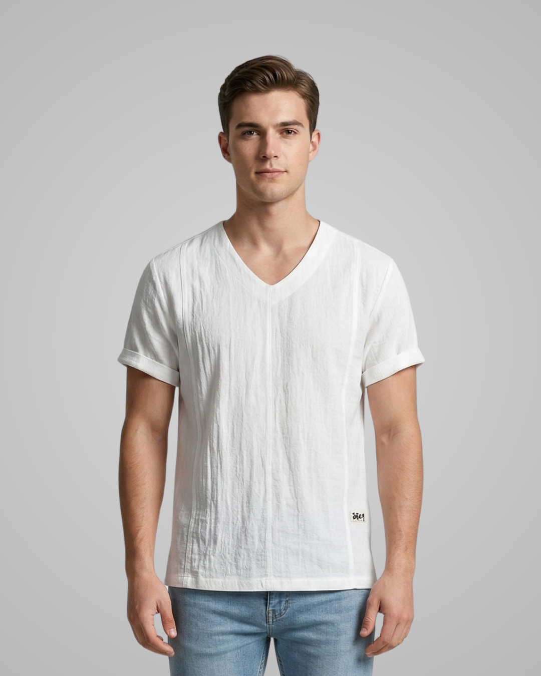Man wearing a white V-neck t-shirt and light blue jeans against a gray background
