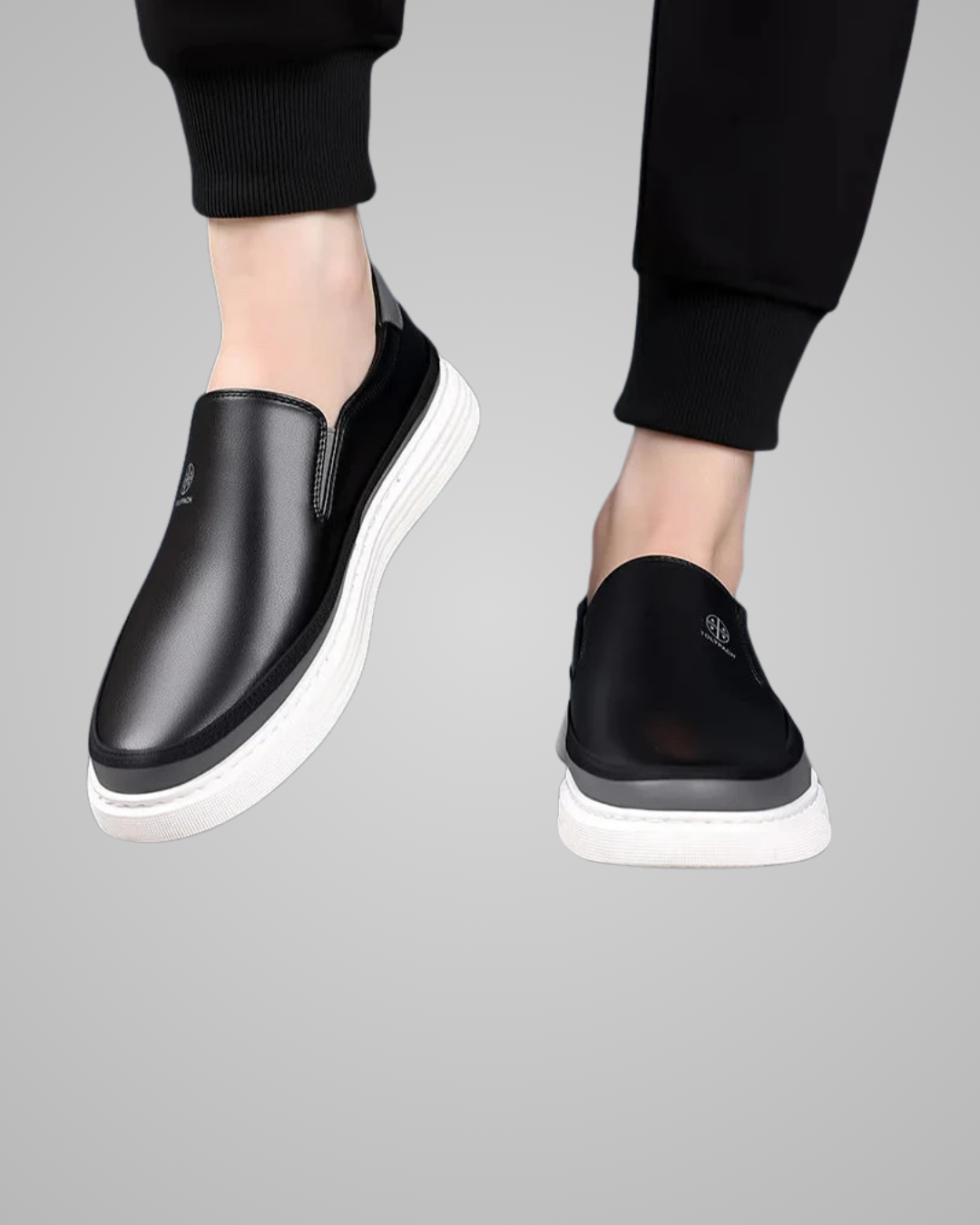Black slip-on shoes with white soles worn by a person on a gray background