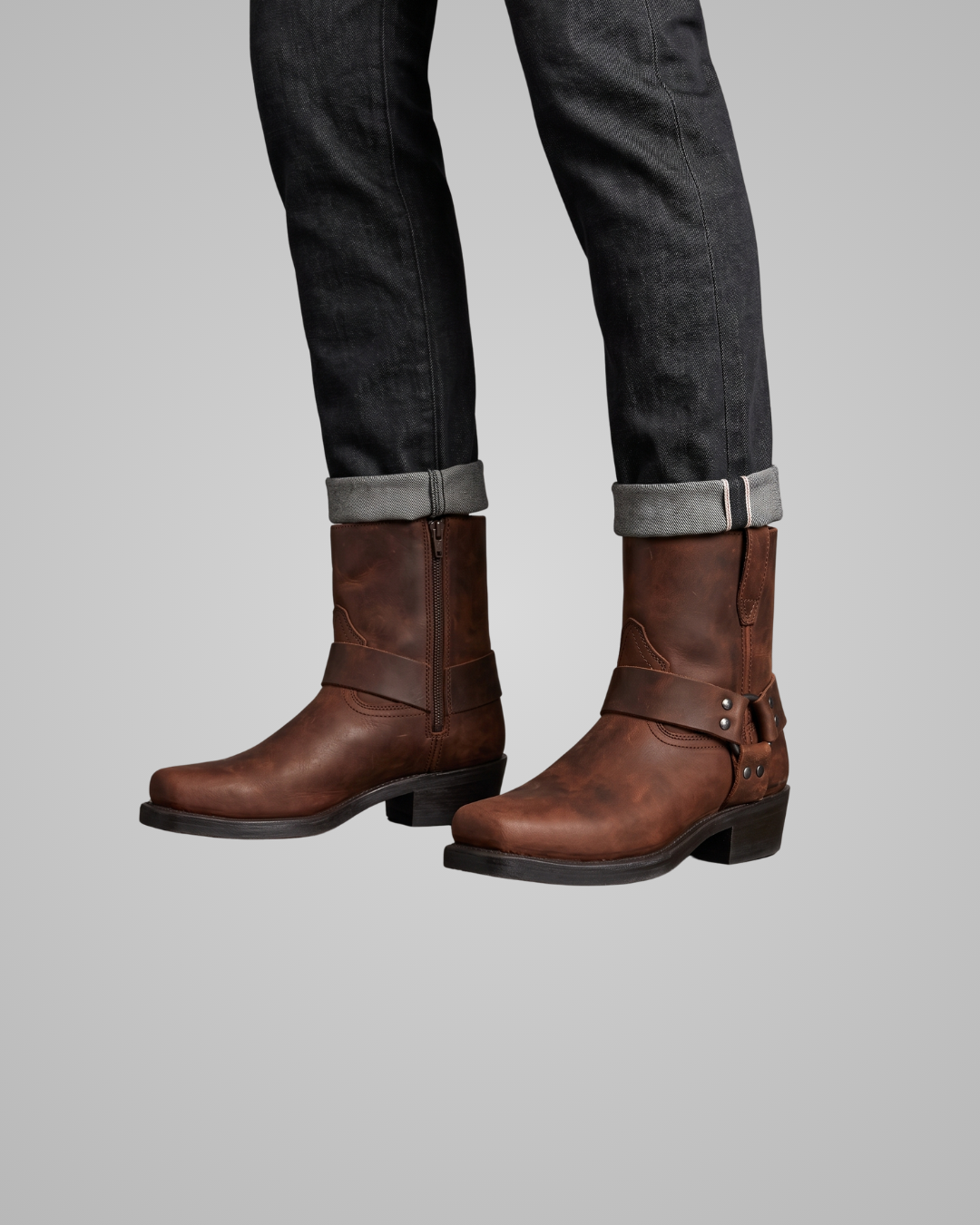 Brown leather boots worn with black jeans on a gray background